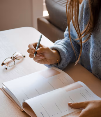 Persona tomando notas en un cuaderno junto a unos lentes